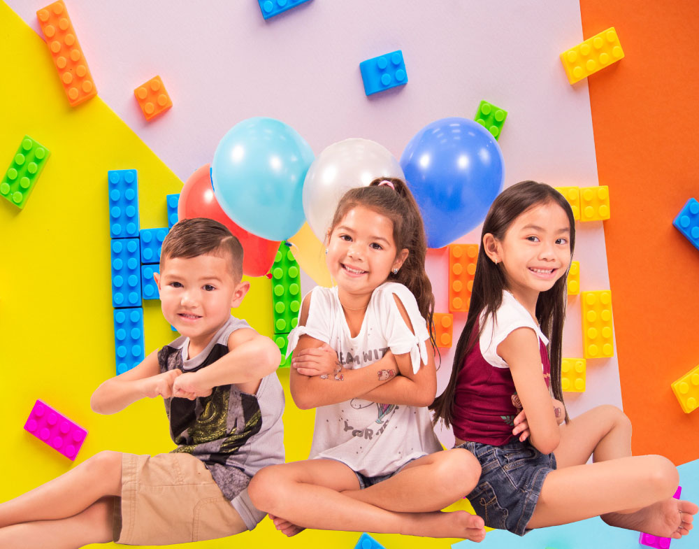 three smiling kids sitting with balloons and large Legos