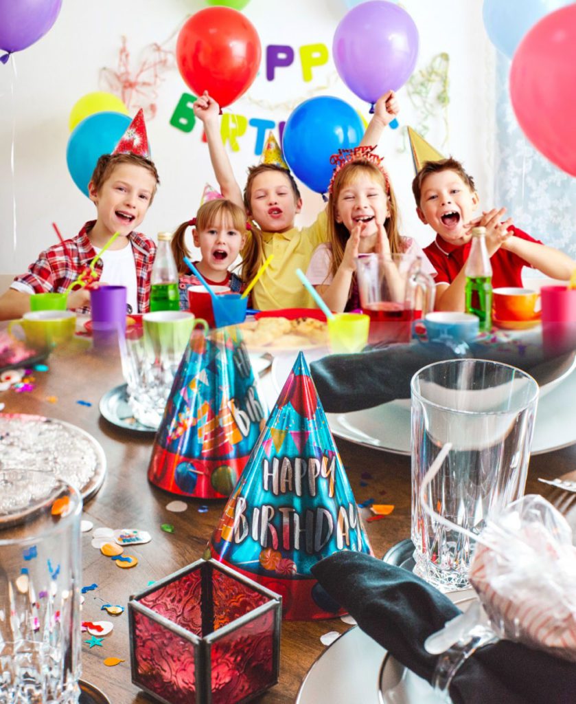 Five happy kids at a birthday party with balloons and colorful hats